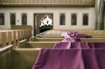 Interior of a row of pews in a church with the purple cloth of the passion spread down the rows