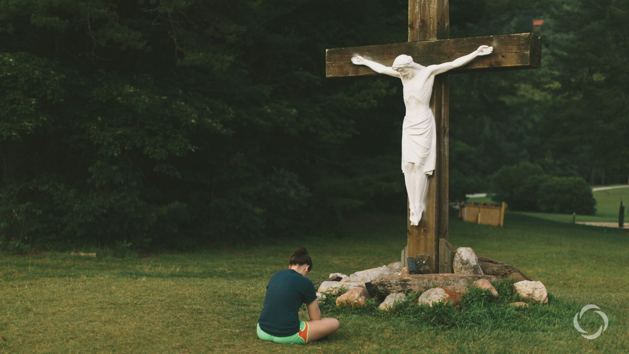 A young teen girl at base of an outdoor cross with lifesize Jesus