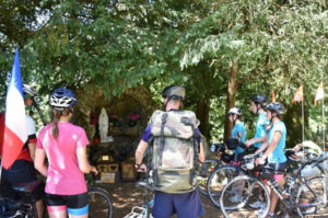 Photo of Day 18 - Our cyclists back on bikes pausing at a grotto of the Virgin Mary