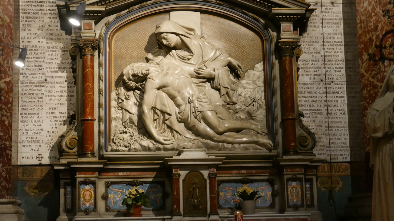 A marblel relief at Notre-Dame des Victoires. The 4th station of the cross, Jesus meets his mother. Some of the 37,000 ex volo plaques surrounding it