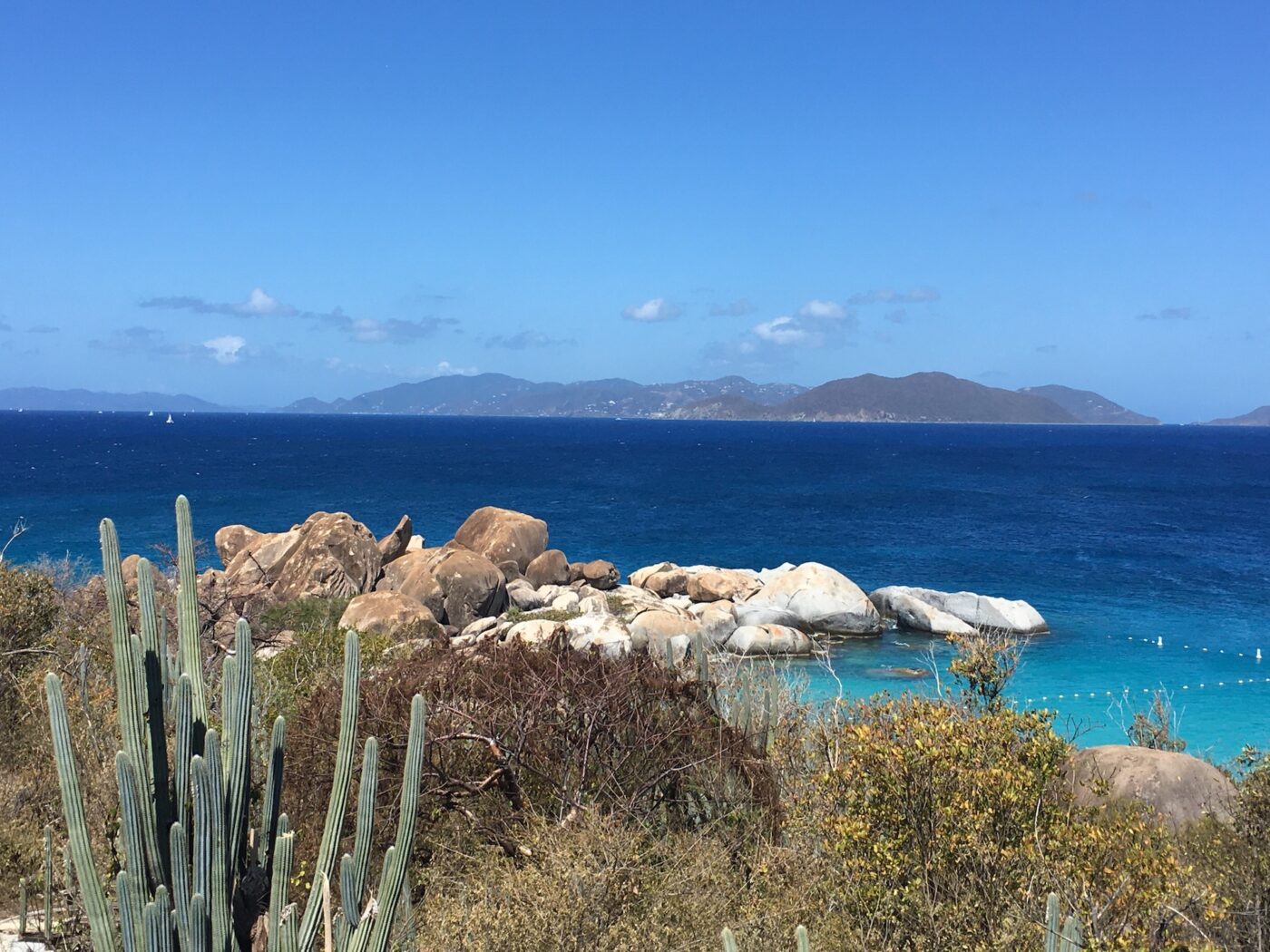 Vista of Caribbean from a rocky shore with desert like cactus in foreground of an unknown island. April, 2022. Beyond is the blue ocean and another island several miles away.