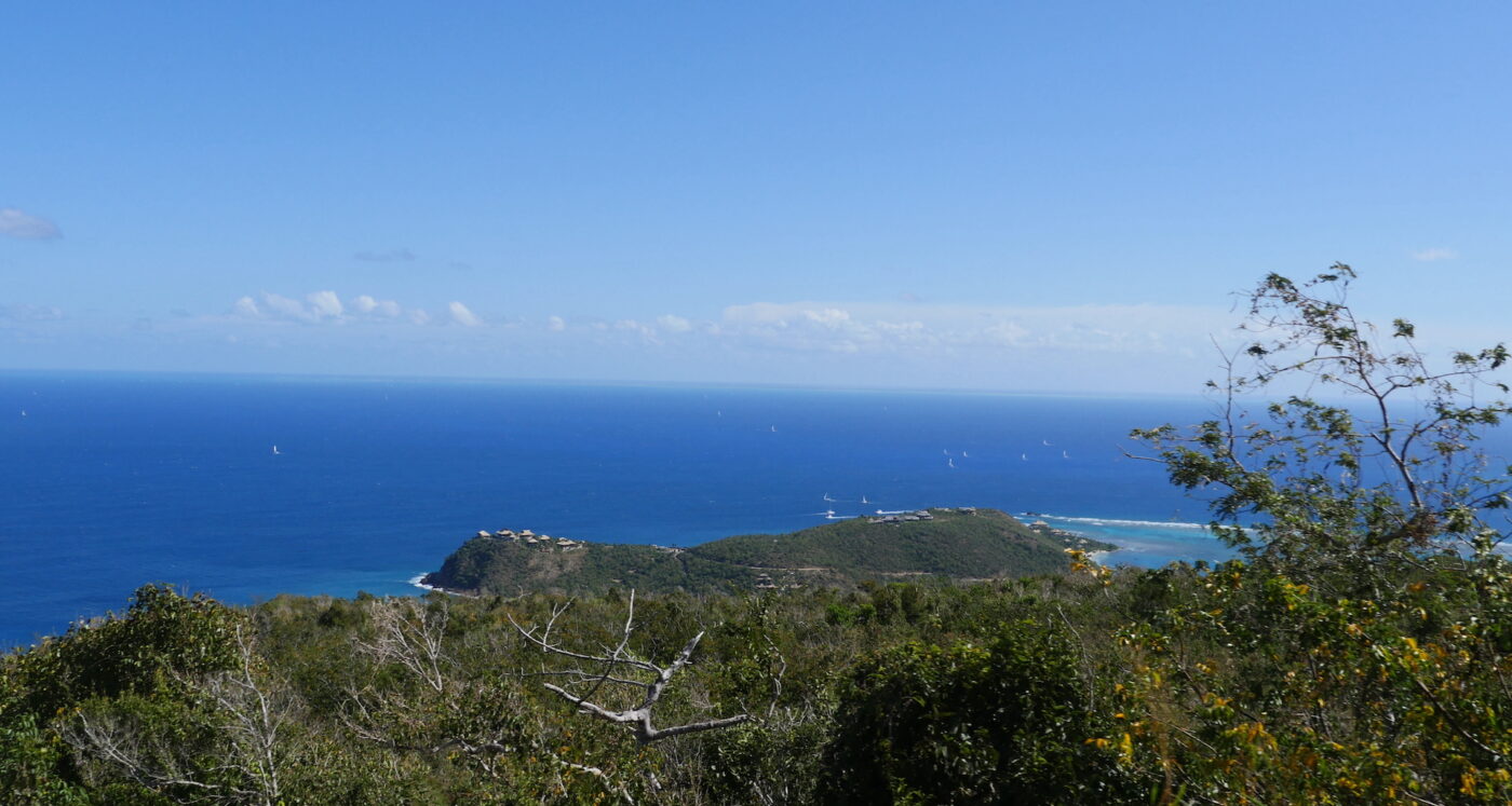 Vista of Caribbean from top of unknown island. April, 2022. Blue ocean and green mountain foliage.